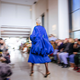 A bright blue dress stands in focus on the runway